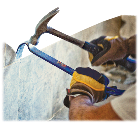 Man with a hammer and pry bar removing wall tile